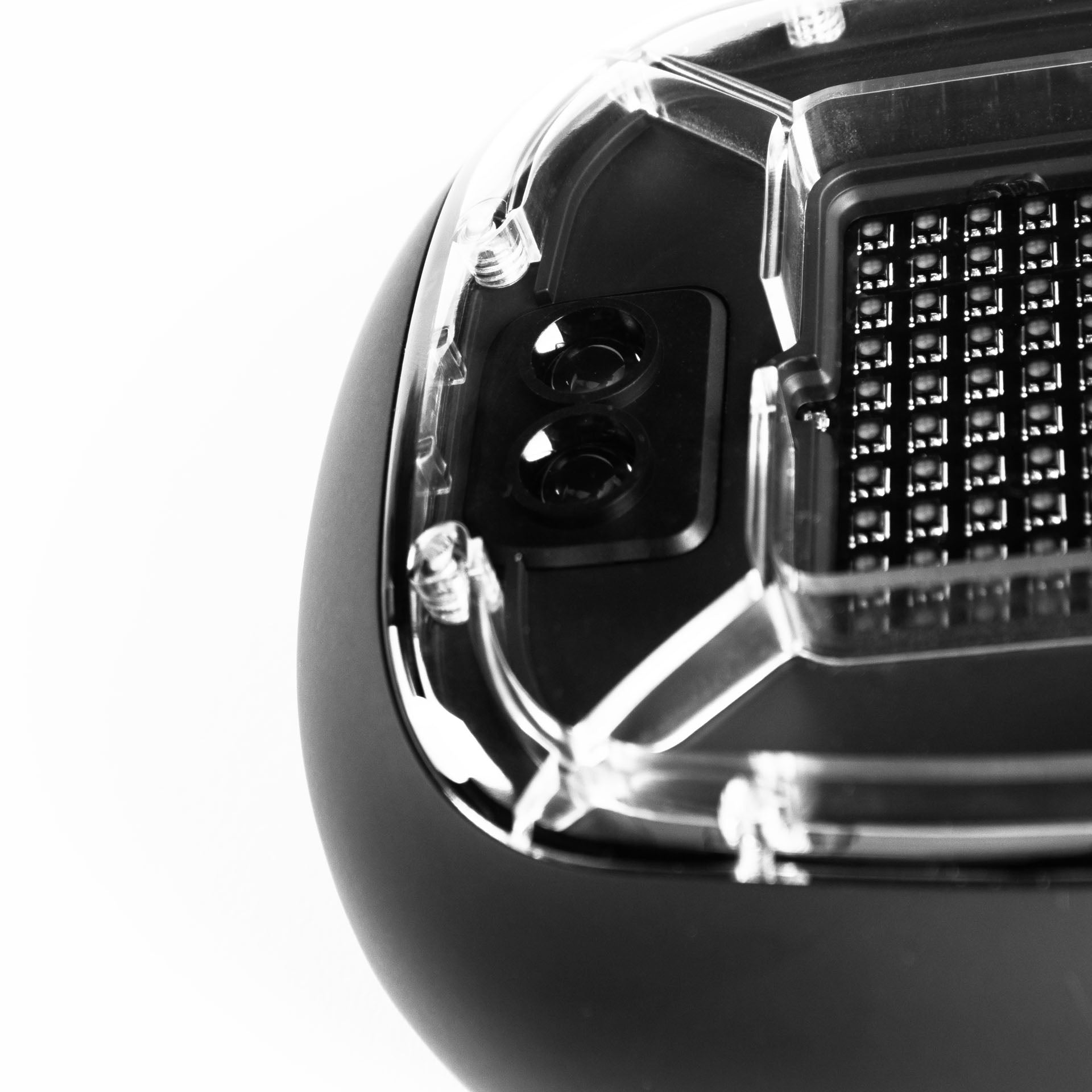 A close-up black and white image of a high-tech device with a robust black exterior and a clear section revealing part of its inner components. There are two circular sensors and a grid of LED lights on the center. The design suggests a durable construction with a modern, sophisticated function, ready for athletic training.